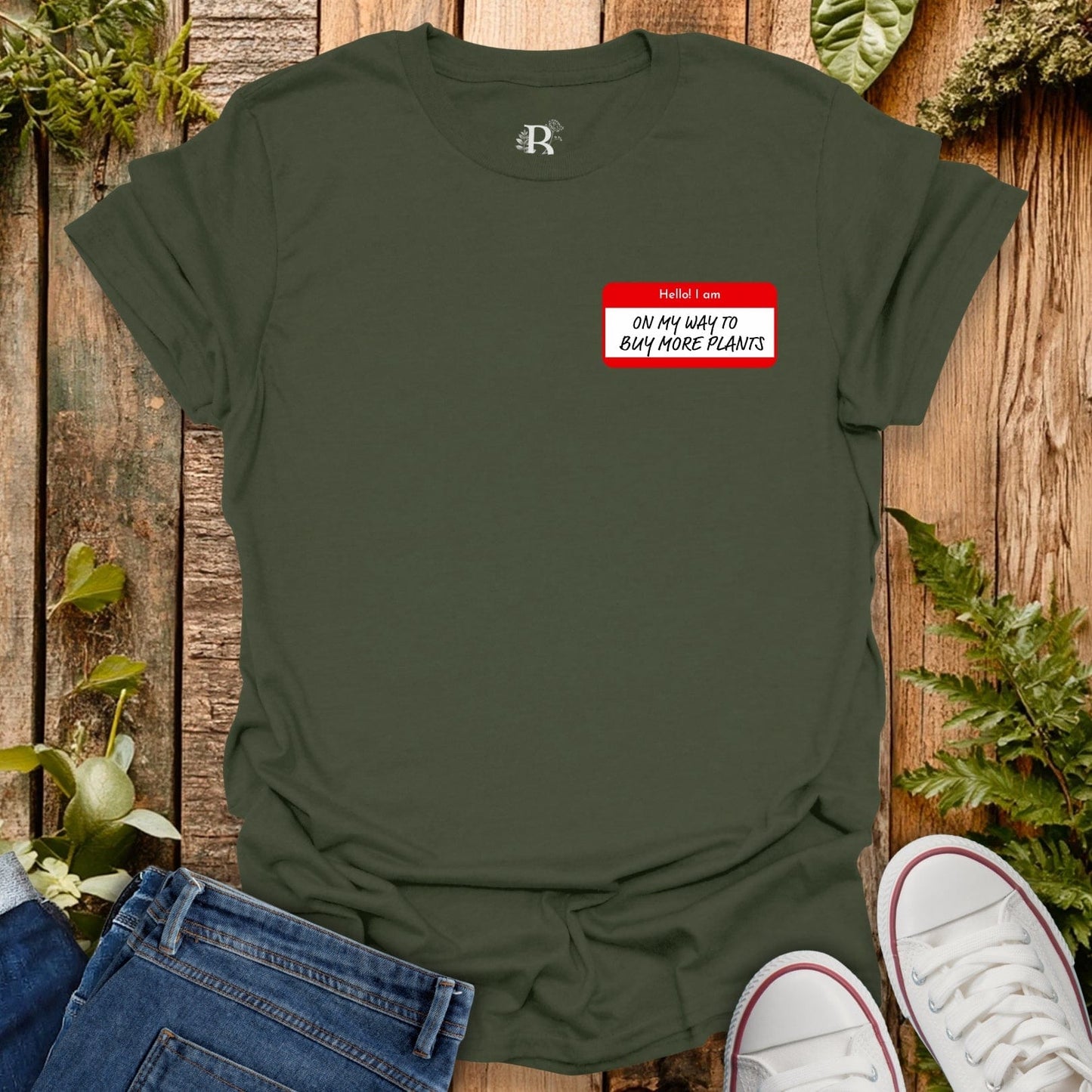 Green t-shirt with a red name tag graphic on a wooden surface with plants.