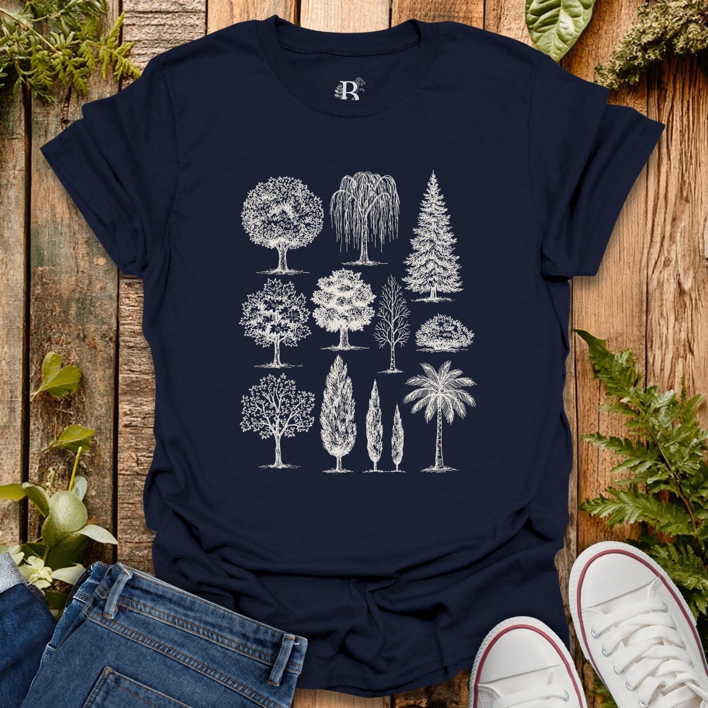 Navy blue t-shirt with white tree illustrations on a wooden surface with plants.