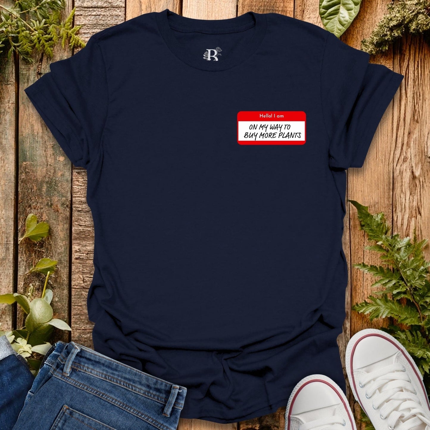 Navy blue t-shirt with a red name tag graphic on a wooden surface with plants.