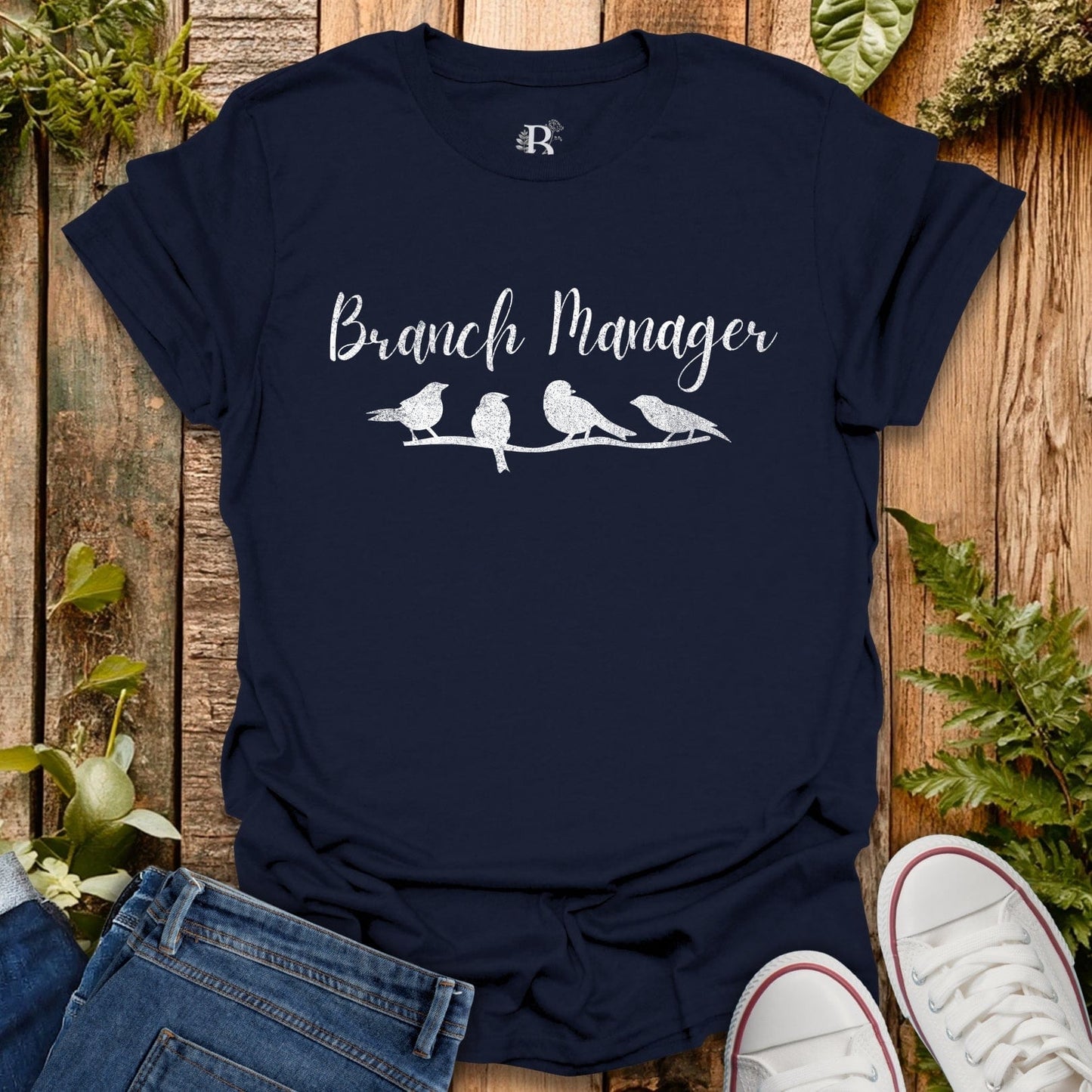 Navy blue t-shirt with 'Branch Manager' and bird design on a wooden surface with plants.