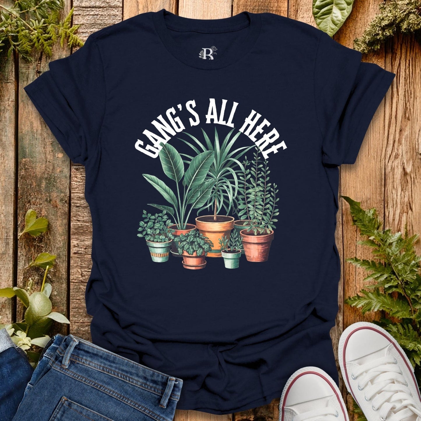 Navy blue t-shirt with plant design and 'Gang's All Here' text on a wooden surface with plants.