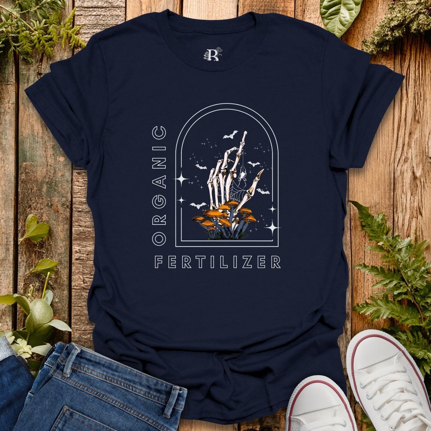 Navy blue t-shirt with skeleton hand and plant design on a wooden surface with plants around.