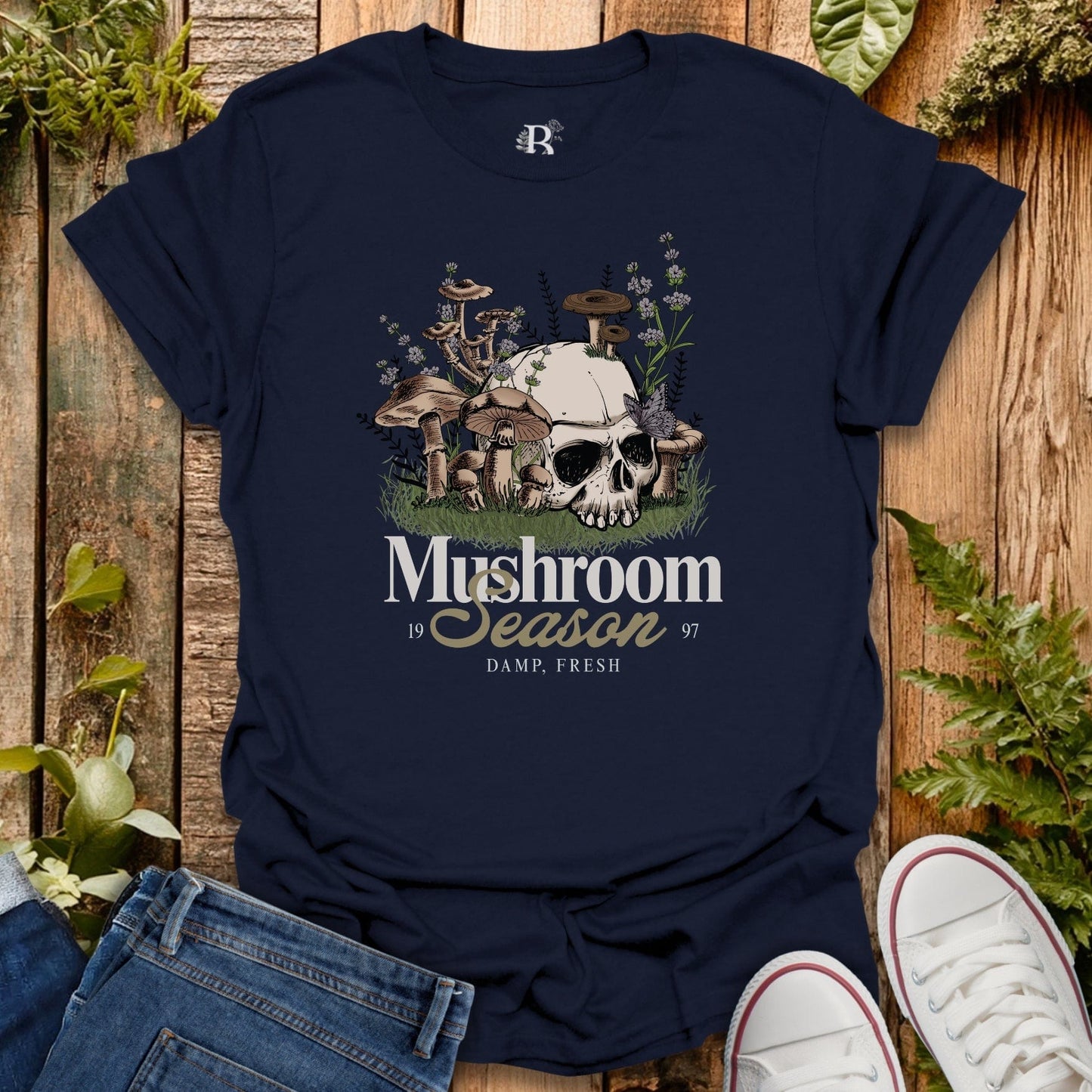 Navy blue t-shirt with mushroom graphic and text on a wooden surface with plants.