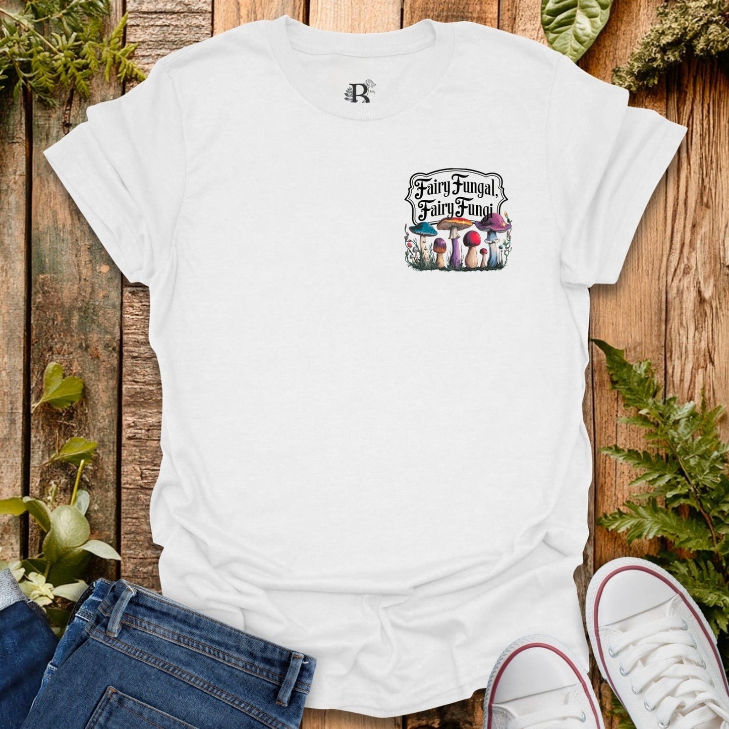 White t-shirt with 'Fairy Fungal' graphic on a wooden surface with plants.