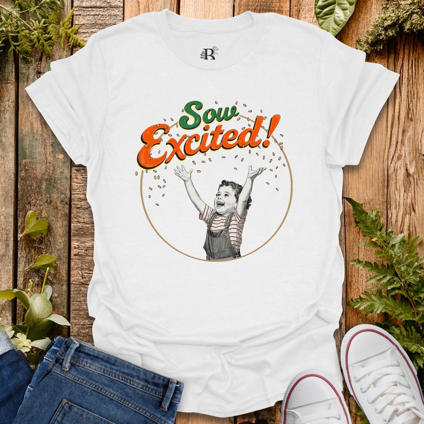White t-shirt with 'Sow Excited!' design on a wooden surface with plants.
