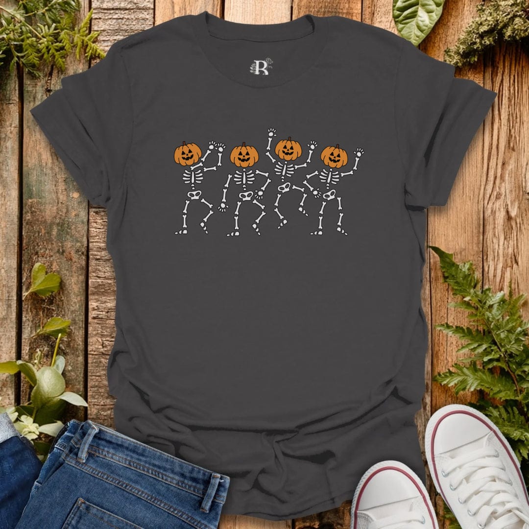 Black t-shirt with skeleton and pumpkin design on a wooden surface with jeans and white sneakers.