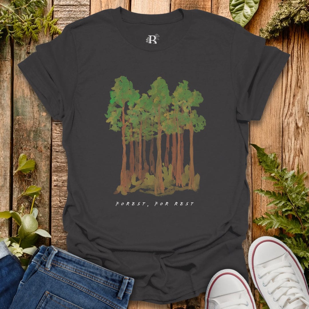 Black t-shirt with forest design and 'Forest, For Rest' text on a wooden background with plants.