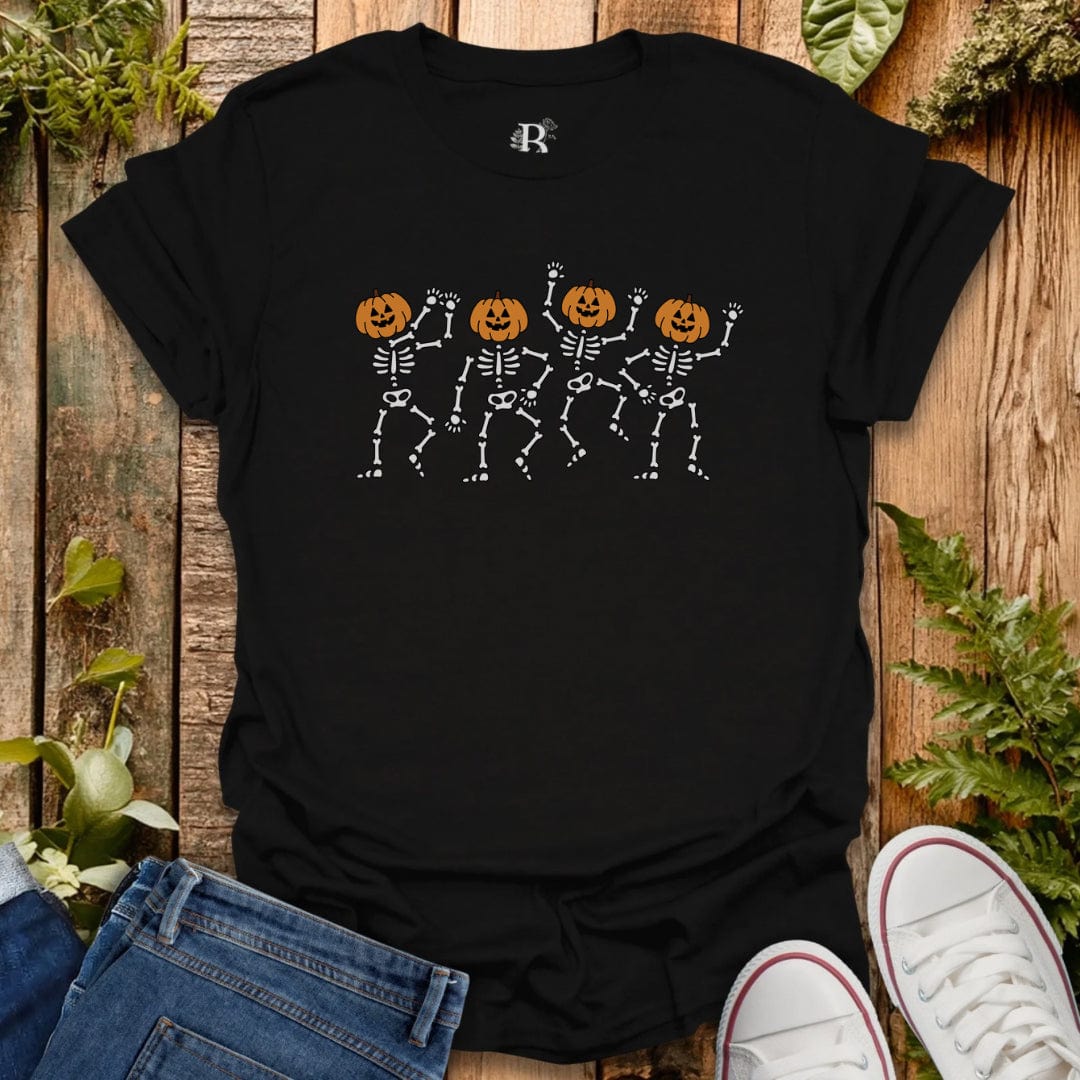 Black t-shirt with skeleton and pumpkin design on a wooden surface with jeans and sneakers.