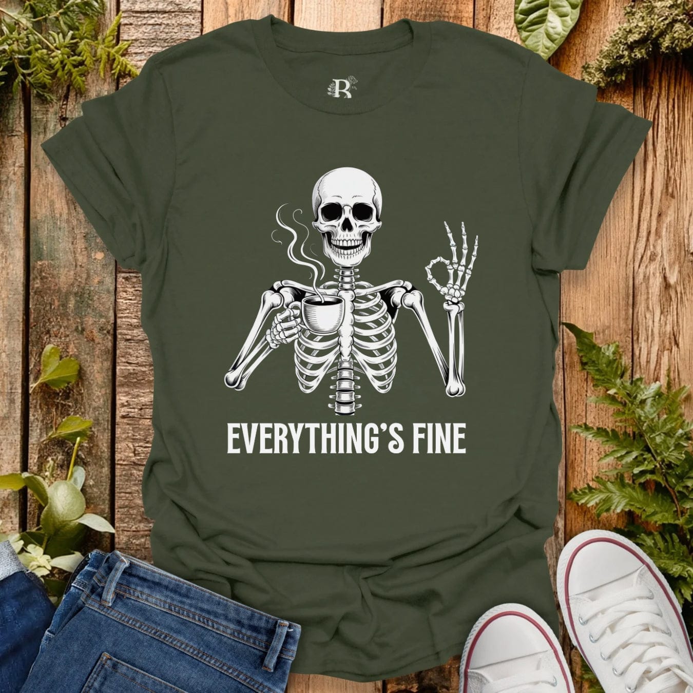 Green t-shirt with skeleton graphic and 'Everything's Fine' text on a wooden surface with jeans and sneakers.