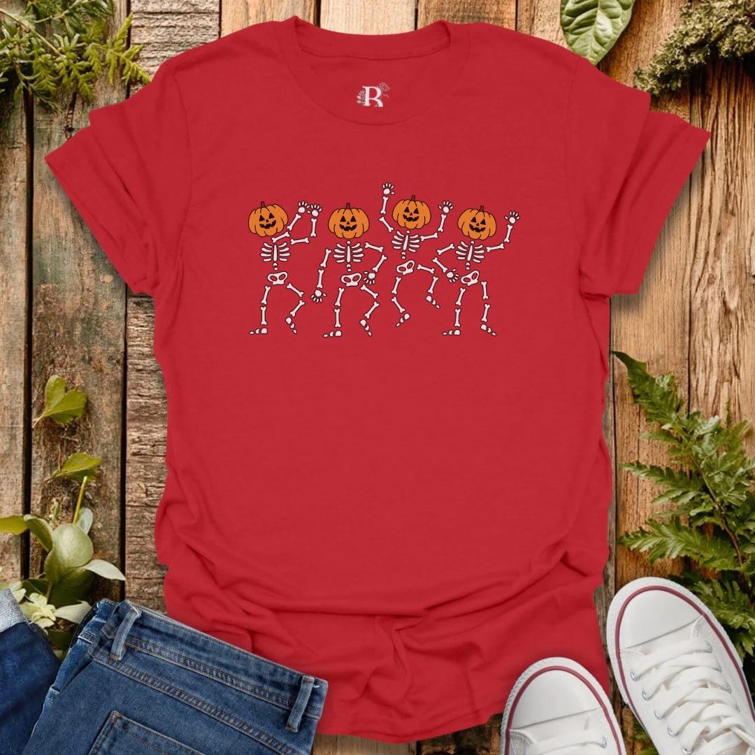 Red t-shirt with skeleton and pumpkin design on a wooden surface with jeans and white sneakers.