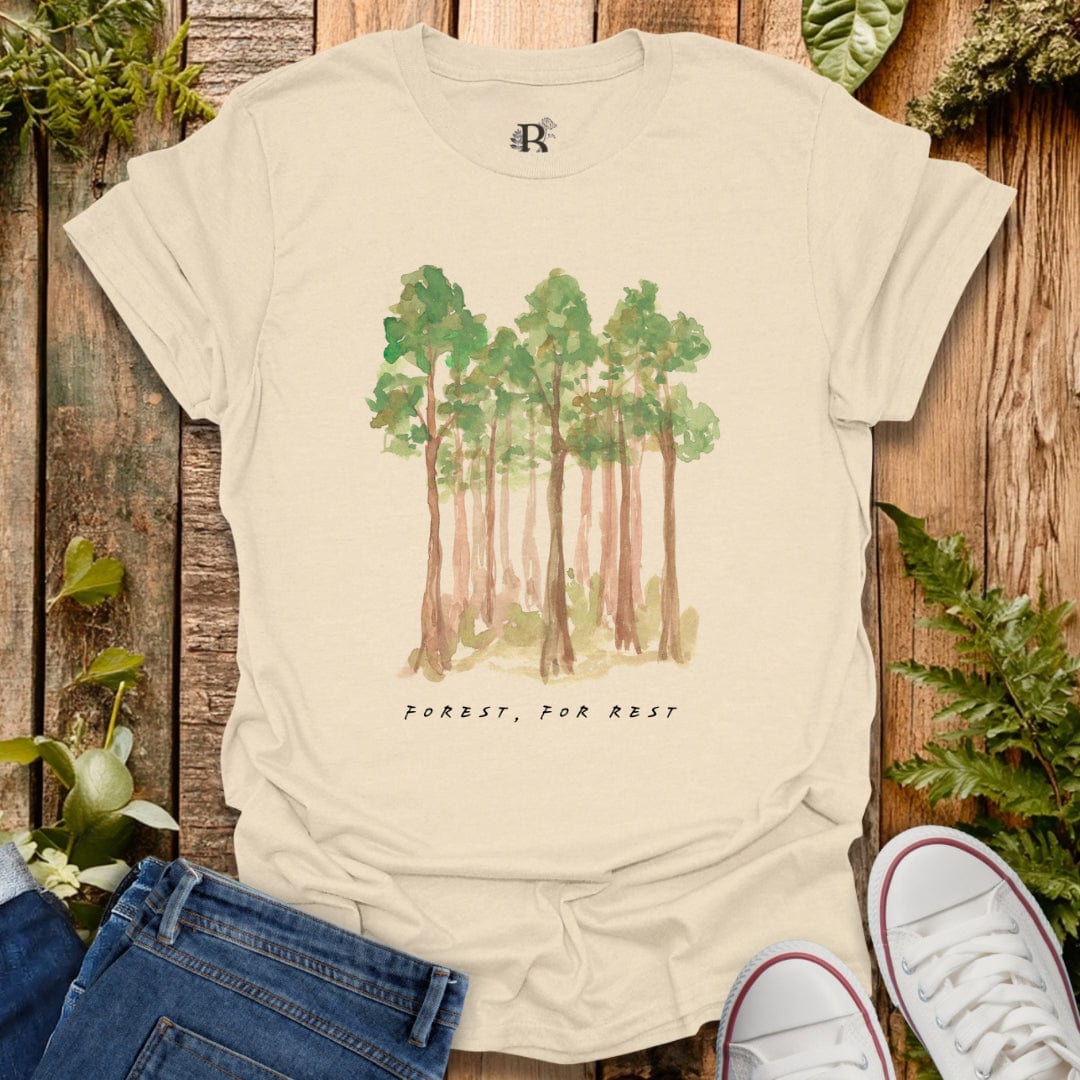 Beige t-shirt with forest graphic and 'Forest, For Rest' text on a wooden background