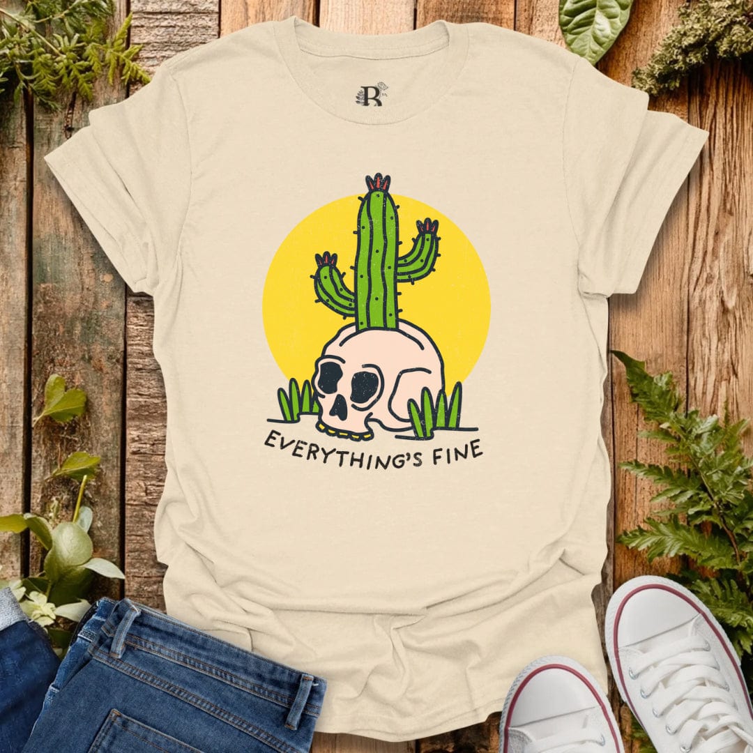 Beige t-shirt with a cactus and skull design and 'Everything's Fine' text on a wooden background.