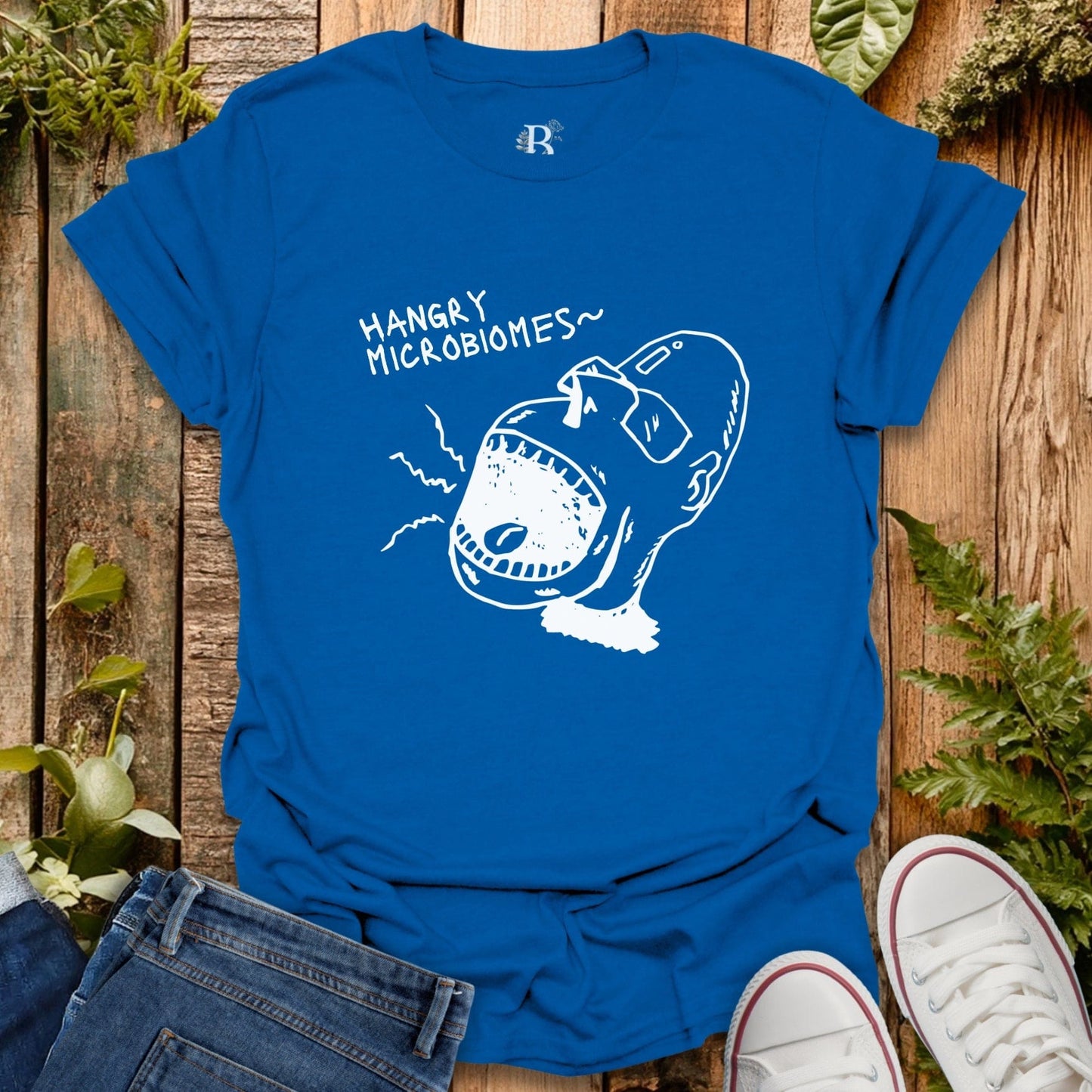 Blue t-shirt with 'Hangry Microbiomes' graphic on a wooden surface with jeans and sneakers.
