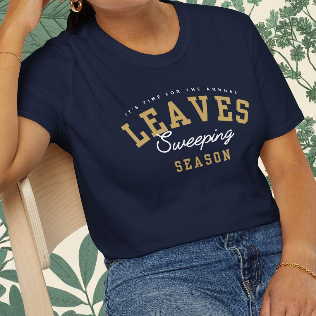 Woman wearing a navy blue t-shirt with 'LEAVES Sweeping Season' text, sitting on a chair.