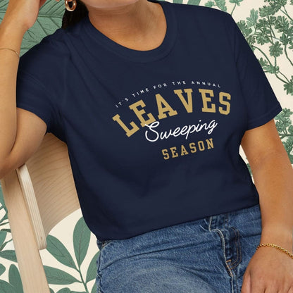 Woman wearing a navy blue t-shirt with 'LEAVES Sweeping Season' text, sitting on a chair.