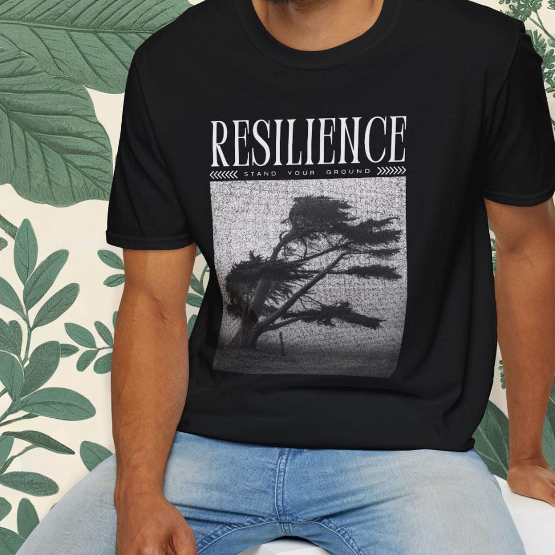 Man wearing a black t-shirt with 'RESILIENCE' text and tree graphic, sitting on a white stool.