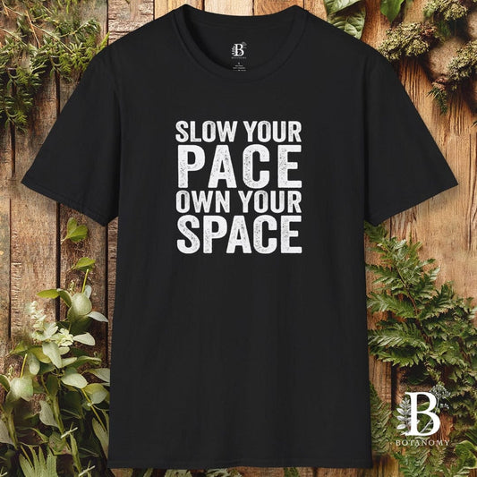 Black t-shirt with 'Slow your pace, own your space' text on a wooden background