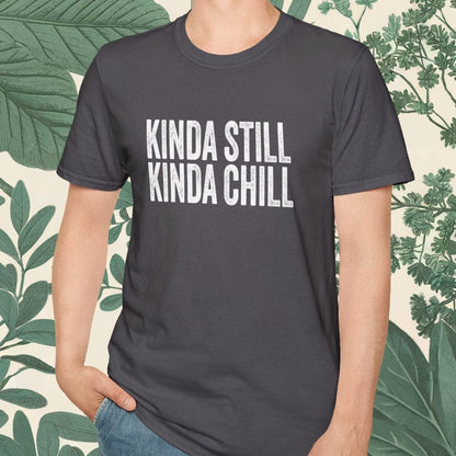 Person wearing a dark gray t-shirt with 'KINDA STILL KINDA CHILL' text, standing against a leafy background.