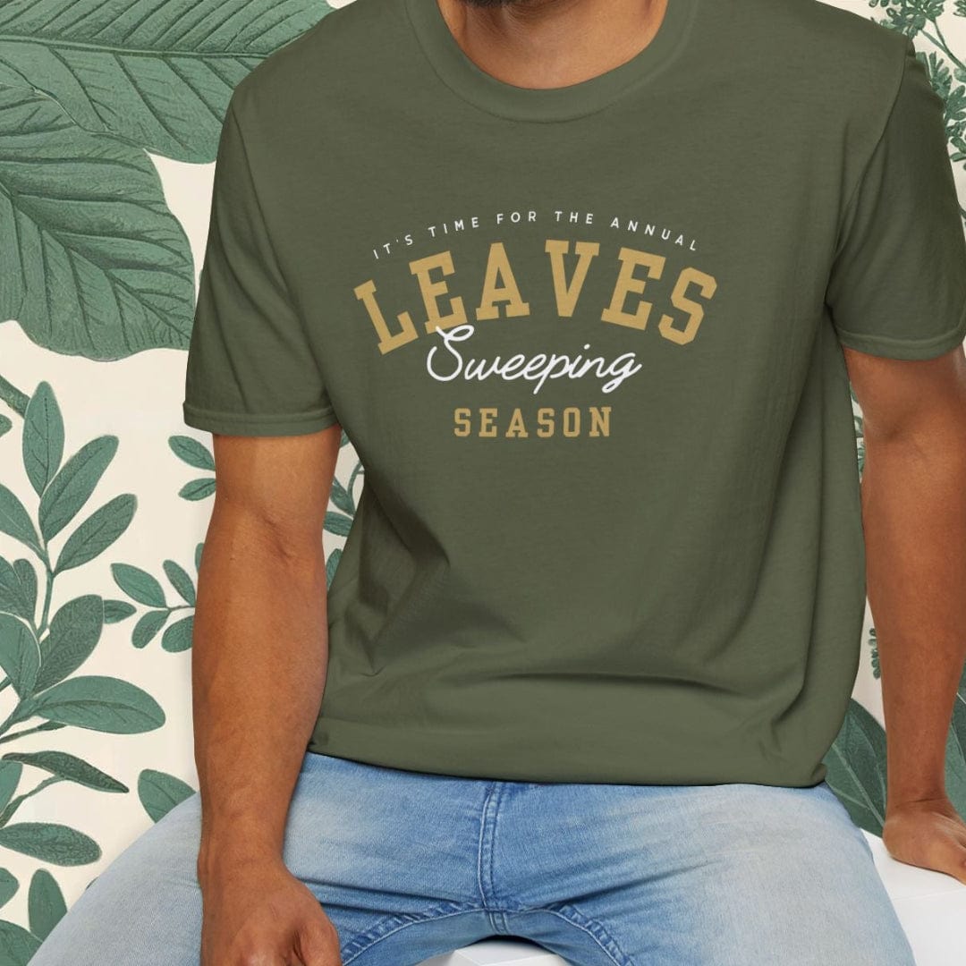 Man wearing a green t-shirt with 'Leaves Sweeping Season' text, sitting on a white stool with a leafy background.