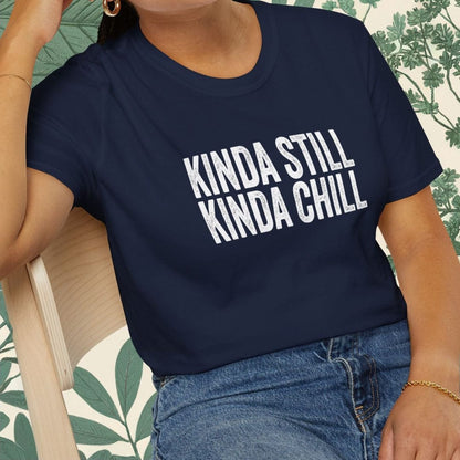 Person wearing a navy blue t-shirt with 'KINDA STILL KINDA CHILL' text, sitting on a chair.