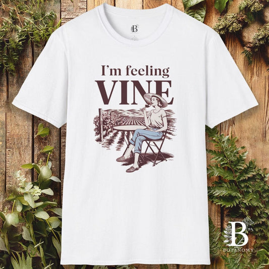 White t-shirt with 'I'm feeling vine' graphic design on a wooden background with plants.