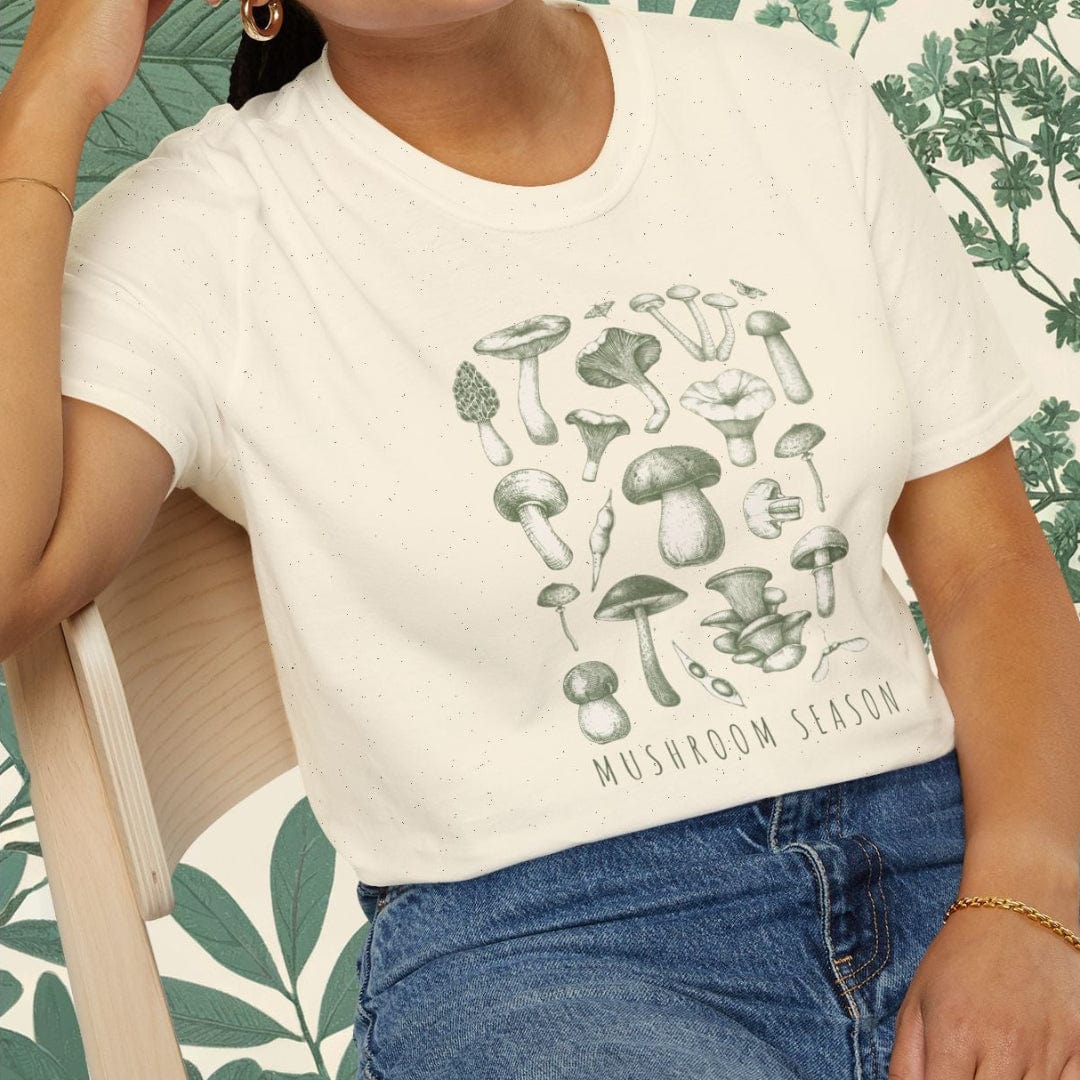 Woman wearing a white t-shirt with mushroom design and blue jeans, sitting on a chair.