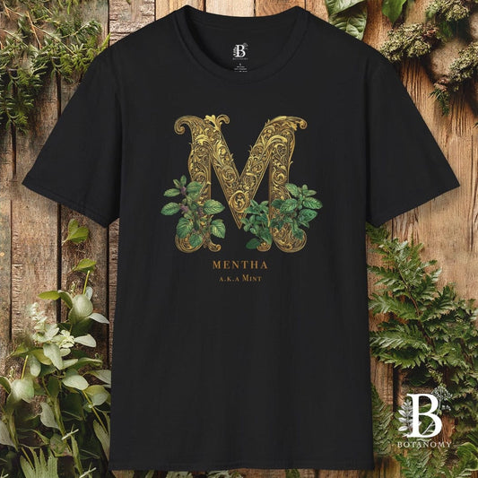 Black t-shirt with decorative 'M' design and plant elements on a wooden background