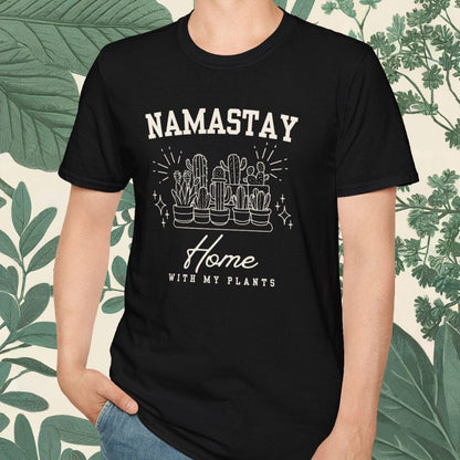 Person wearing a black t-shirt with 'NAMASTAY Home With My Plants' text and graphic, standing against a leafy background.