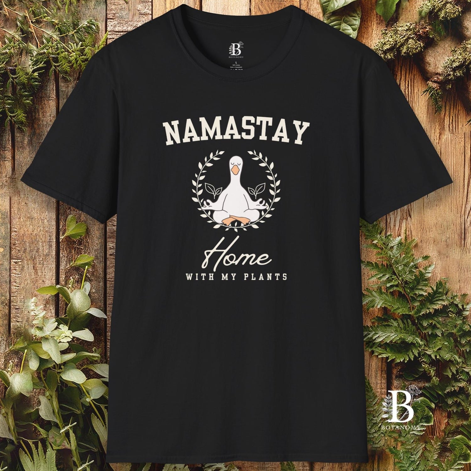 Black t-shirt with 'Namastay Home with My Plants' design on a wooden background with plants.