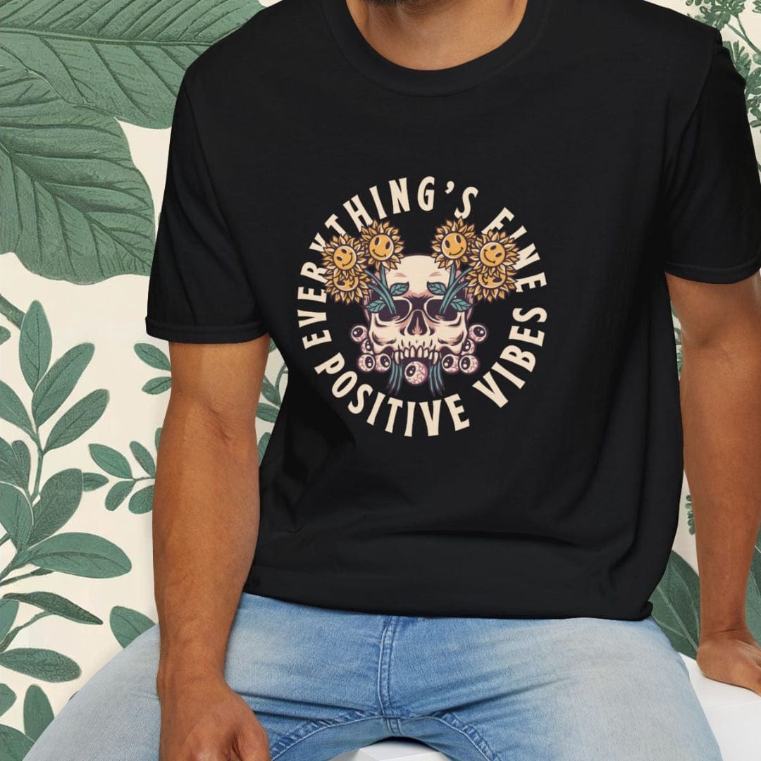 Man wearing a black t-shirt with a graphic design and text, sitting on a white stool with a green leafy background.