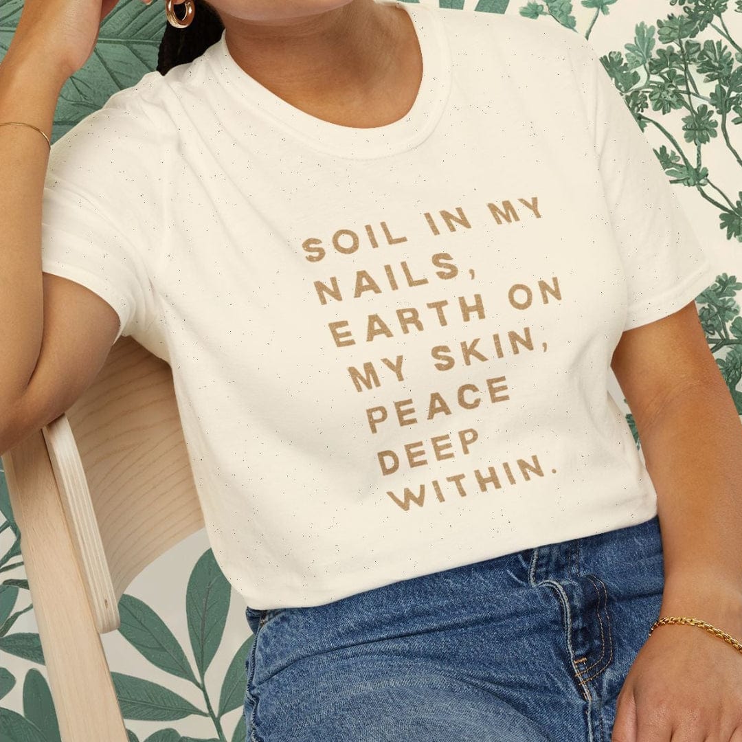 Woman wearing a white t-shirt with text, sitting on a chair with a green leafy background