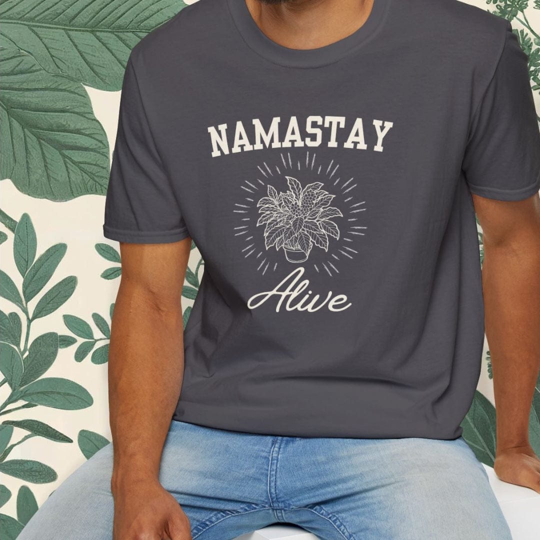 Man wearing a dark gray t-shirt with 'NAMASTAY Alive' text and floral design, sitting on a white stool against a light background.