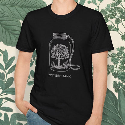 Person wearing a black t-shirt with a graphic design of an oxygen tank and tree, standing against a leafy green background.