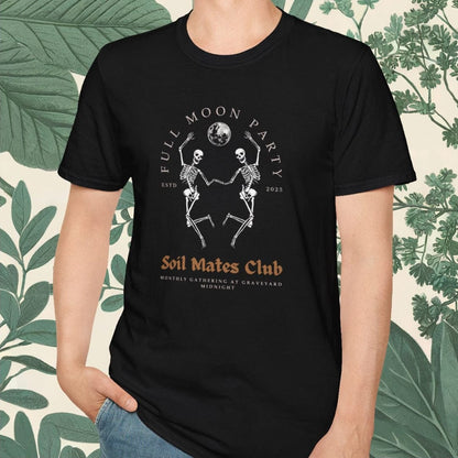 Person wearing a black t-shirt with graphic design and text, standing against a decorative background with green leaves.