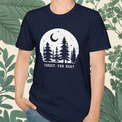 Person wearing a navy blue t-shirt with a forest design and text, standing against a leafy background.