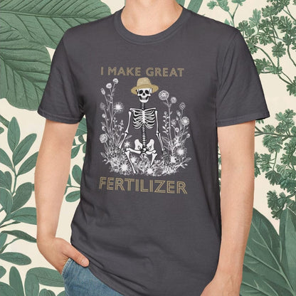 Person wearing a dark gray t-shirt with a graphic design and text, standing against a leafy background.