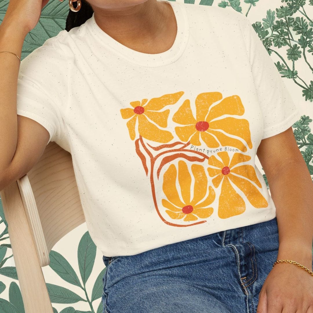 Woman wearing a white t-shirt with orange floral design and blue jeans, sitting on a chair.