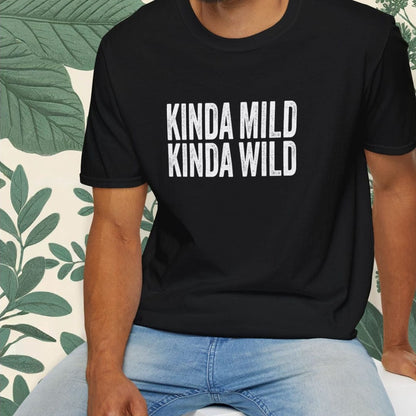 Man wearing a black t-shirt with 'KINDA MILD KINDA WILD' text, sitting on a white stool with a green leafy background.