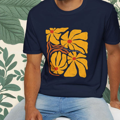Man wearing a navy blue t-shirt with a yellow floral design, sitting on a white stool against a white background.