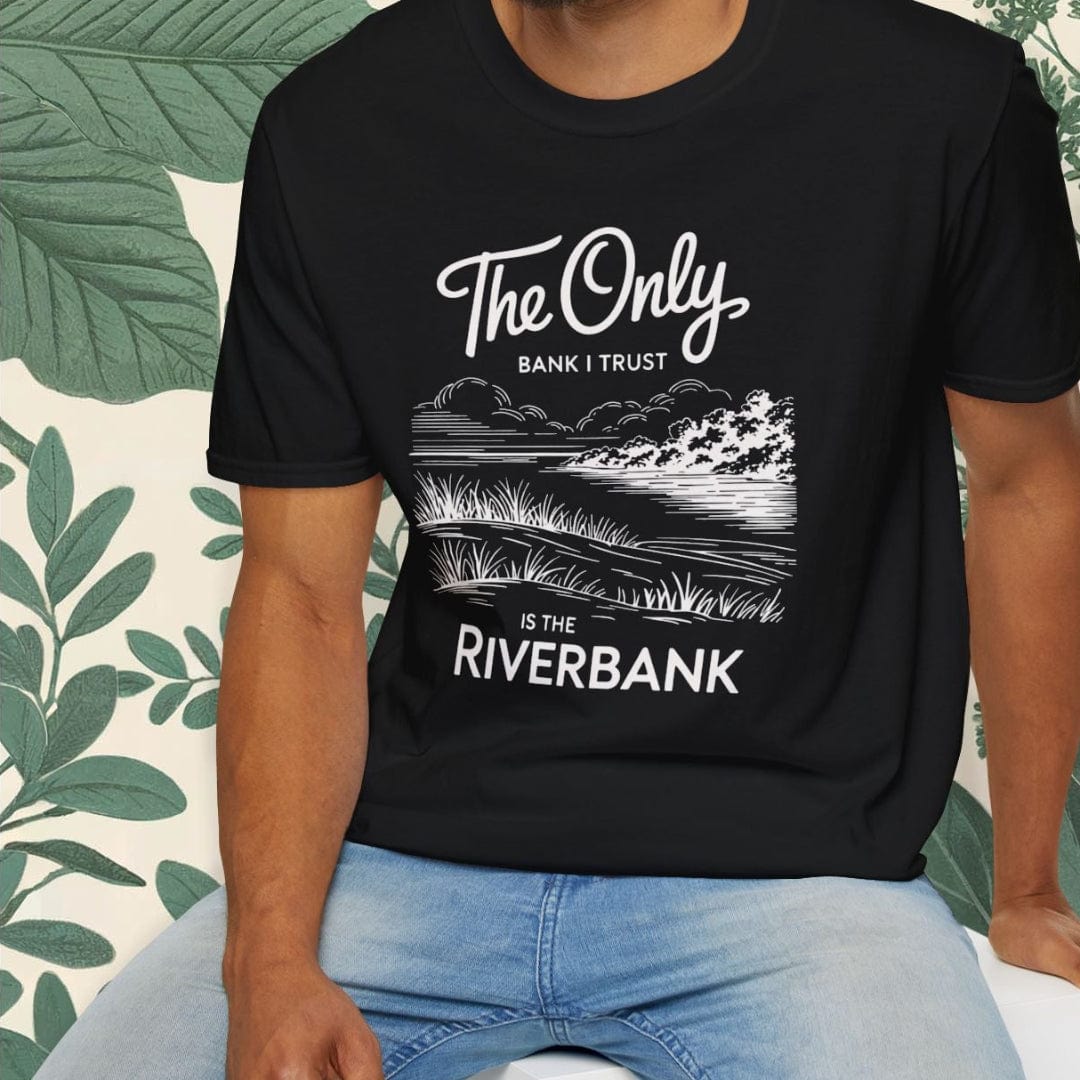 Man wearing a black t-shirt with text and graphics, sitting on a white stool with a green leafy background.