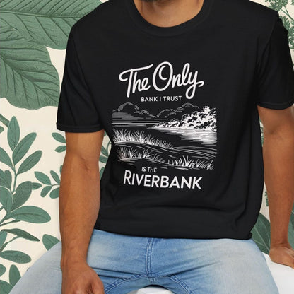 Man wearing a black t-shirt with text and graphics, sitting on a white stool with a green leafy background.