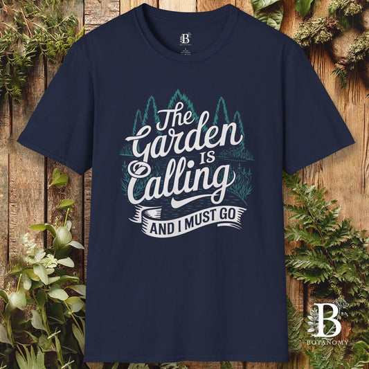 Navy blue t-shirt with 'The Garden is Calling' text on a wooden background with plants.