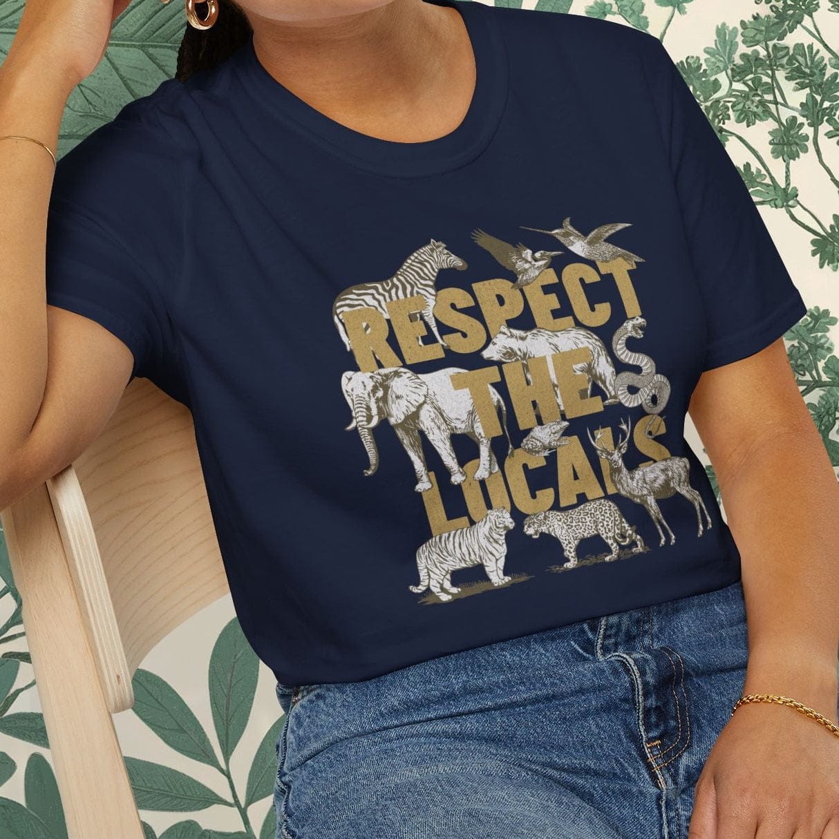 Woman wearing a navy blue t-shirt with 'Respect the Locals' graphic design, sitting on a chair.