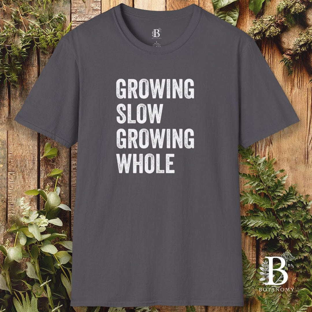 Gray t-shirt with 'Growing Slow Growing Whole' text on a wooden background with plants.
