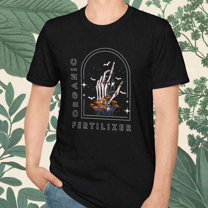 Person wearing a black t-shirt with graphic design and text, standing against a leafy background