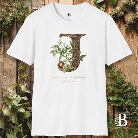 White t-shirt with decorative letter 'J' design on a wooden background with greenery