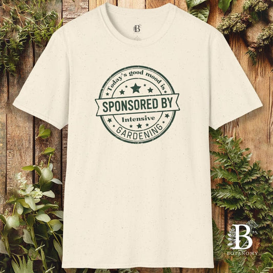 White t-shirt with 'Sponsored by Intensive Gardening' text on a wooden background with plants.