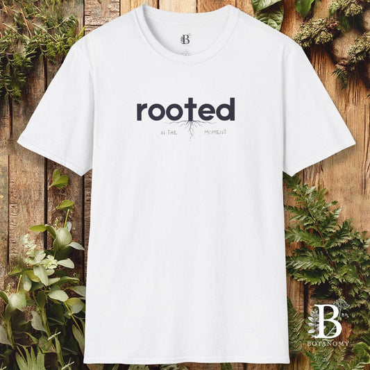 White t-shirt with 'rooted' text on a wooden background with plants