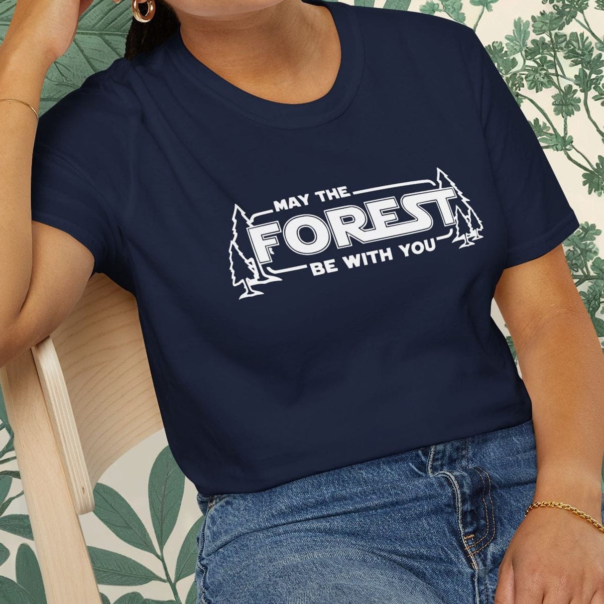 Person wearing a navy blue t-shirt with 'May the Forest be with you' text, sitting on a chair.