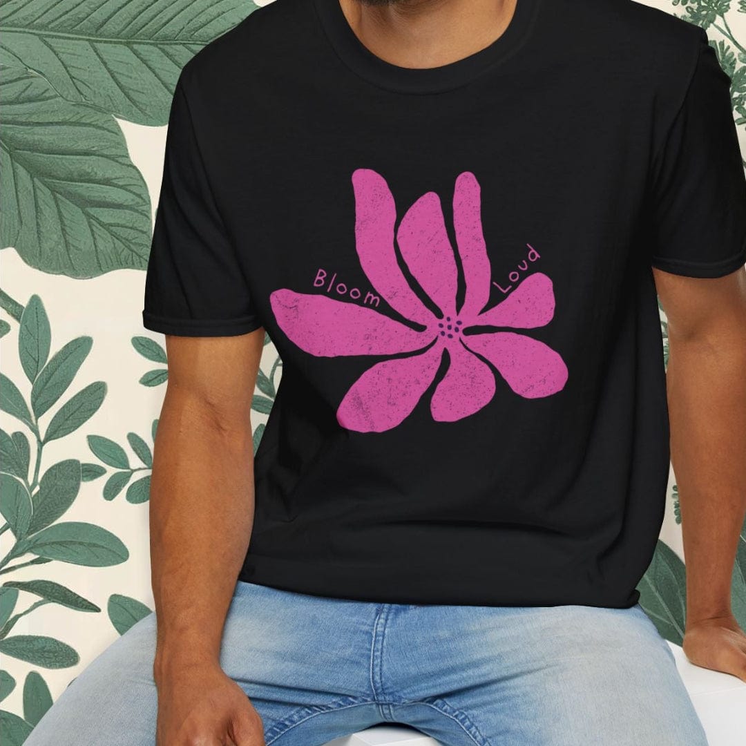 Man wearing a black t-shirt with a pink flower design, sitting on a white stool with a green leafy background.